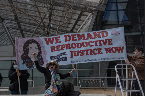 protester raises a fist in front of We Demand Reproductive Justice Now banner