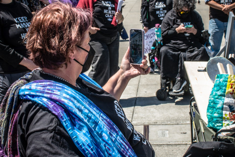 woman with bright blue scarf in wheelchair films people take free black t-shirts from a box