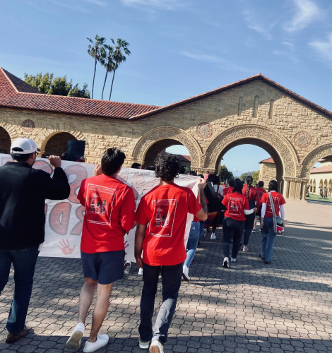 view from rear...students in red t-shirts march near iconic stanford arch