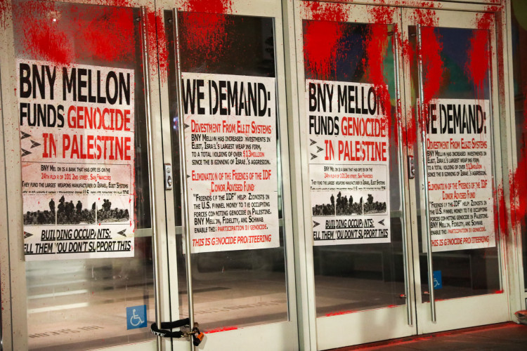 posters wheatpasted on the entrance with one reading 'BNY MELLON FUNDS GENOCIDE IN PALESTINE' and another reading 'WE DEMAND DIVESTMENT FROM ELBIT SYSTEM ELIMINATION OF THE FRIENDS OF THE IDF DONOR ADVISED FUND'