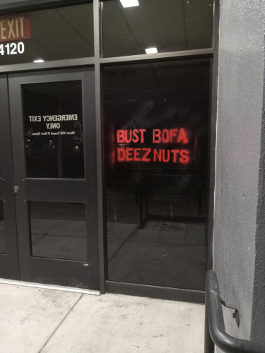 A stencil spraypainted on the door of a Bank of America that reads "BUST BOFA DEEZ NUTS."