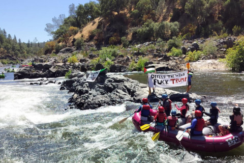 Rafters passing a banner that says “defend the wild, fuck trump”