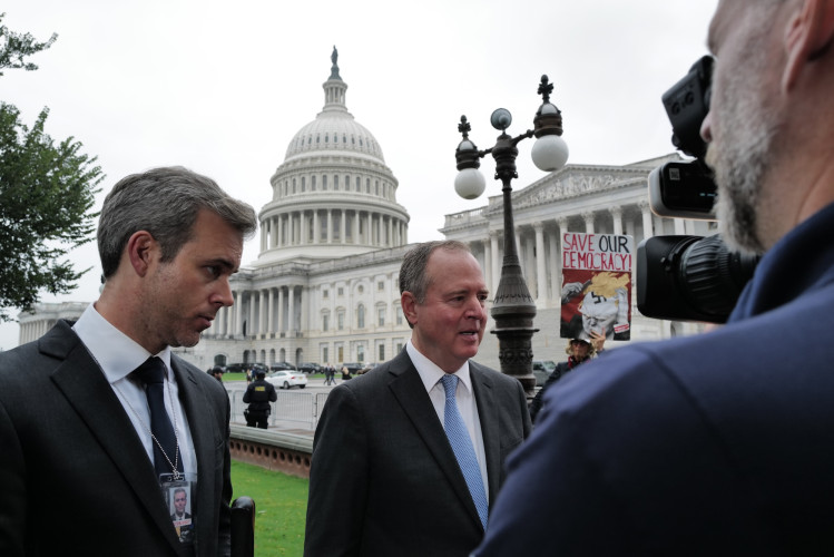 U.S. Senator Adam Schiff (D-CA), speaks with the press while an activist holds a sign warning of the loss of democracy.