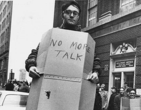 Photo of man holding cardboard sign that reads, "No More Talk,"  from the 1970 nationwide wildcat strike of American postal workers