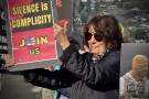 Woman holding sign that says "Silence is Complicity. Join us"