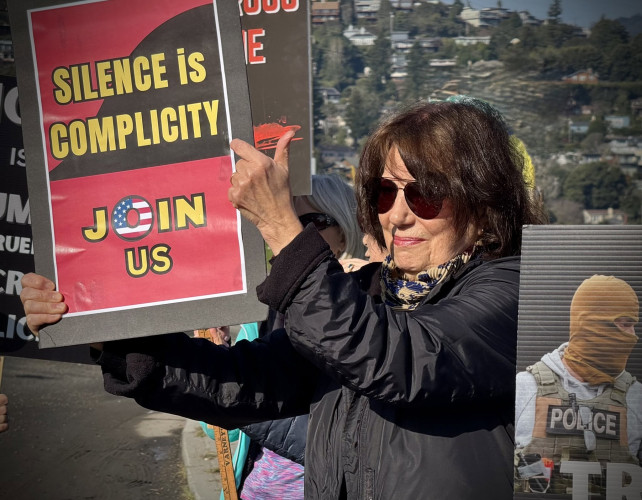 Woman holding sign that says "Silence is Complicity. Join us"