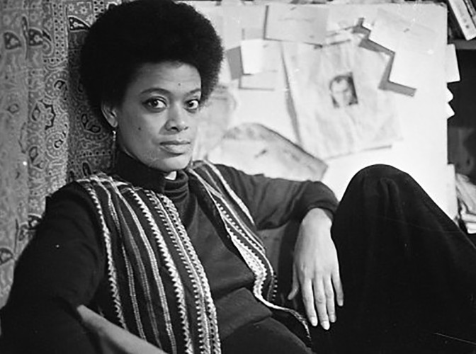Toni sitting leaning on a wall, looking front with left hand resting on left knee